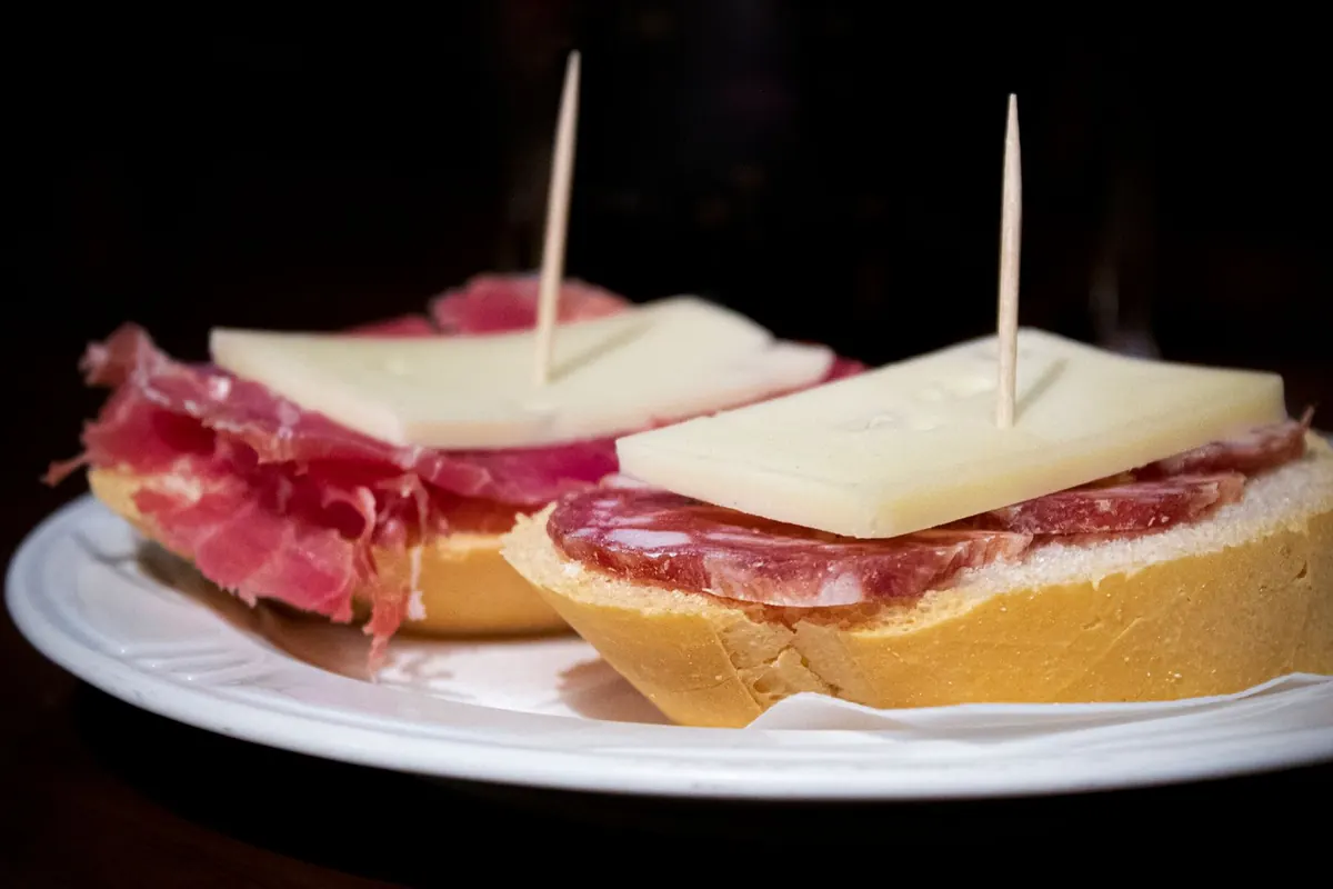 Small open sandwiches with cured meat and cheese on a white plate