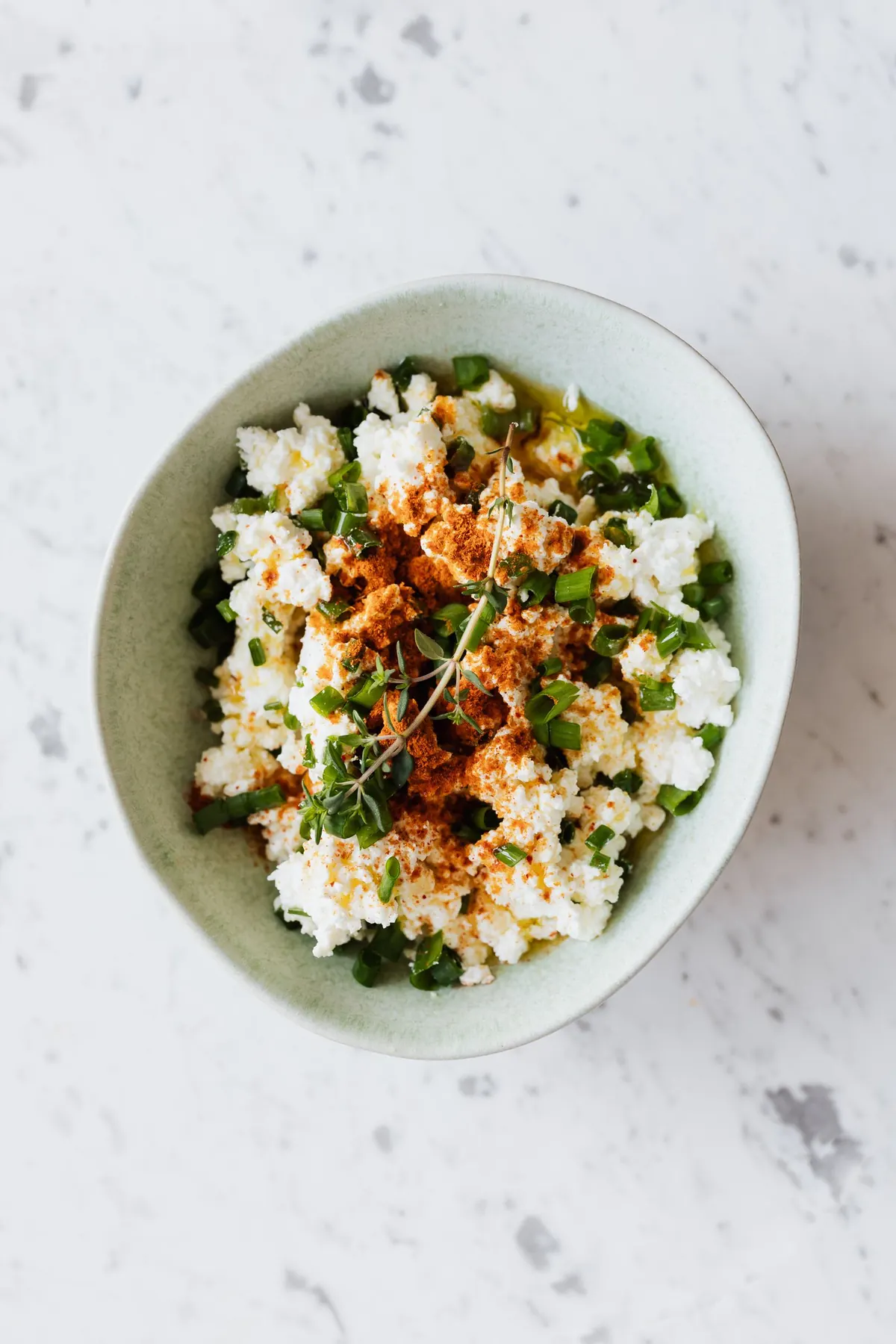 A bowl of cottage cheese topped with chopped fresh herbs