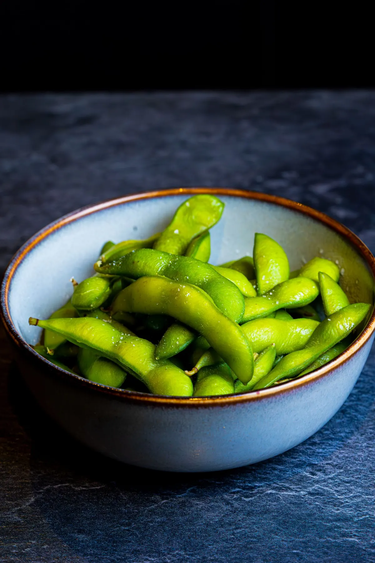 Bright green edamame beans in their pods in a pale blue ceramic bowl